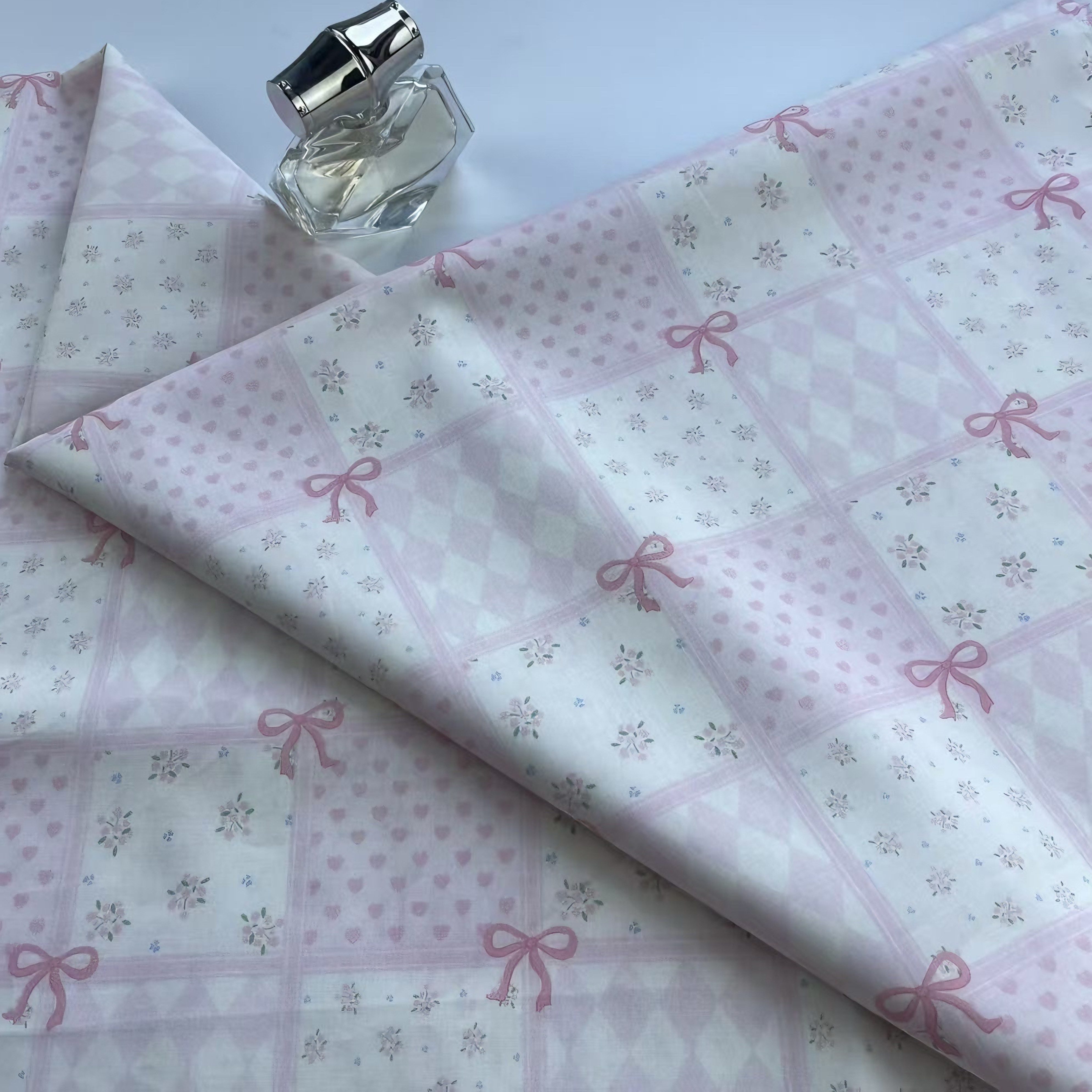 パステル ピンクにインスピレーションを得た、リボン ハートと花のモチーフの綿 100% 生地。DIY ファッションやホーム テキスタイル プロジェクトに最適です。